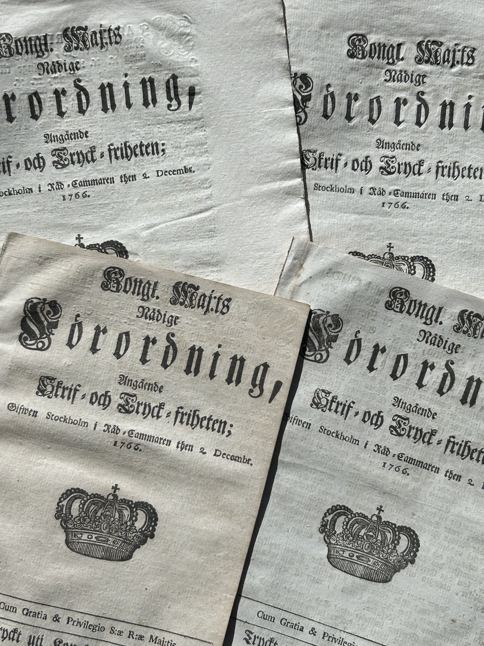 Närbild i svartvitt av flera historiska tryck med äldre typografi och riksvapen.